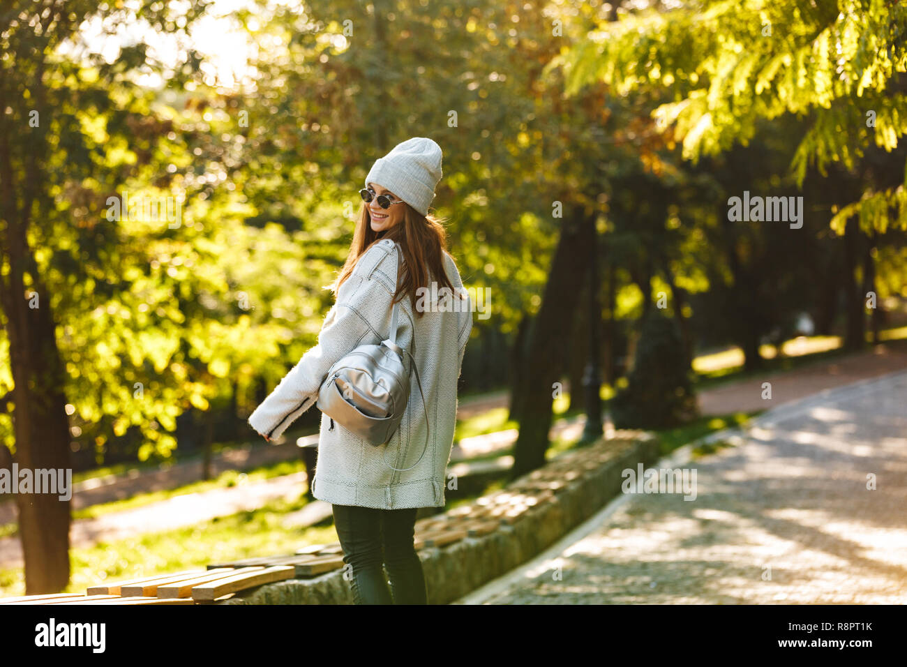 Cheerful young woman dressed in autumn coat and hat walking outdoors at the city street Stock Photo
