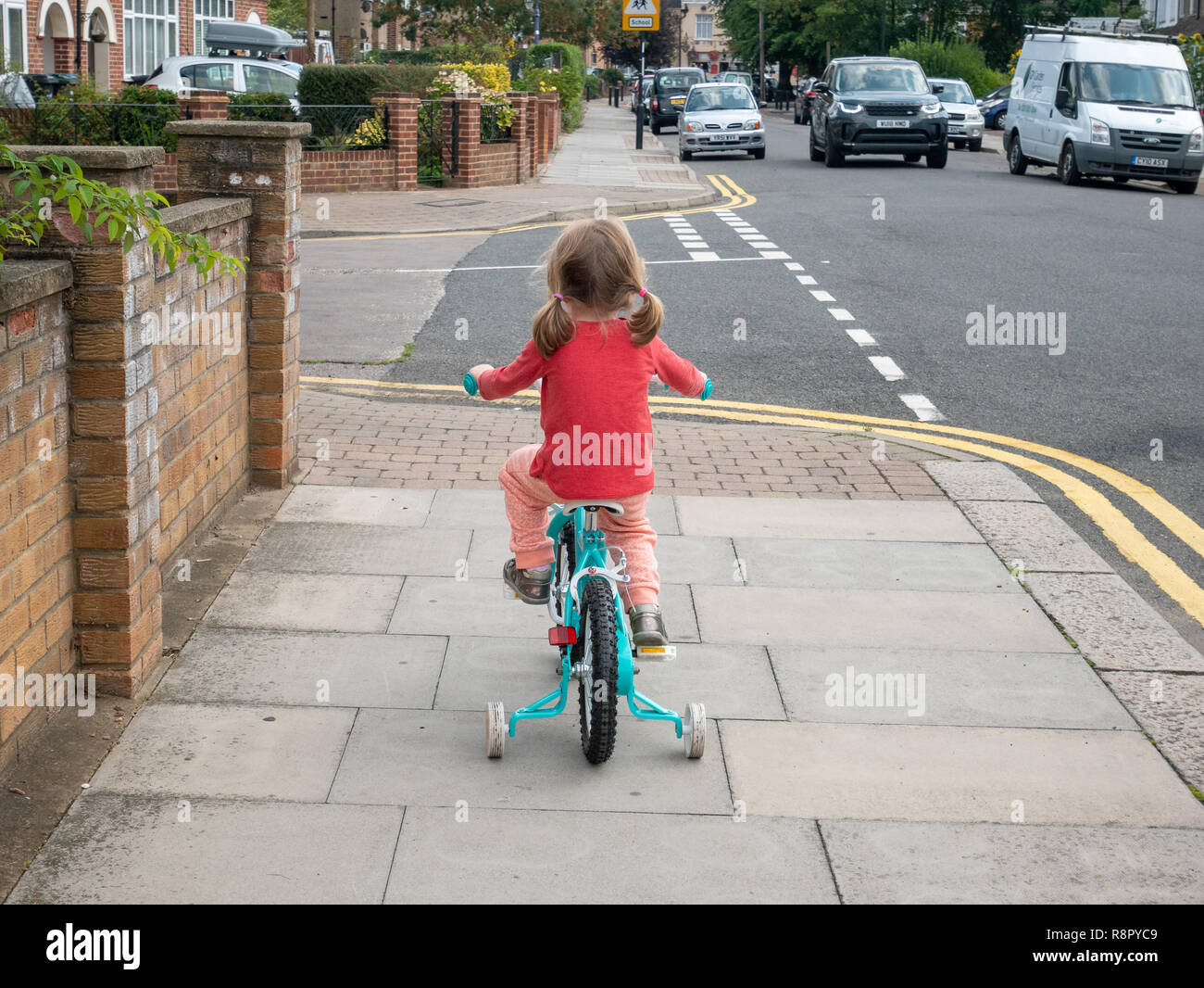 Small child riding her bicycle with stabilisers, UK, London Stock Photo