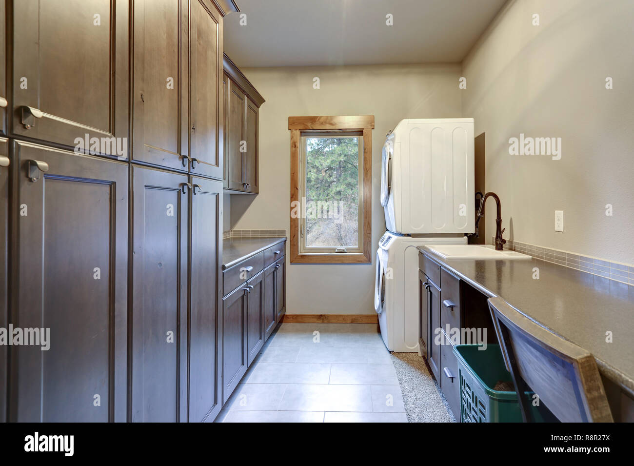 Laundry room with a stacked white front loading washer and dryer, floor to ceiling dark shaker cabinets. Stock Photo