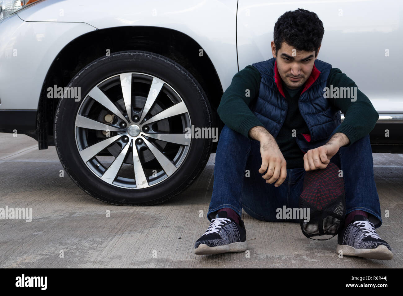 depressed man sitting on a ground leaning on his broken car. Sad, angry and frustrated person. Emergency. Stock Photo