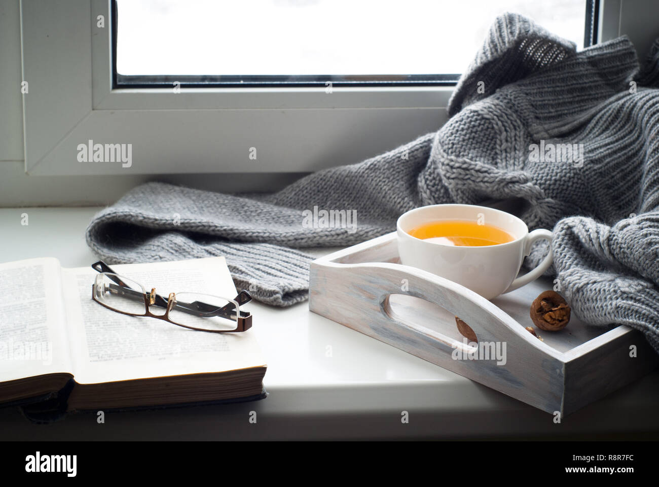 A cup of hot tea in white cup and book on the windowsill. Winter relax concept. Stock Photo