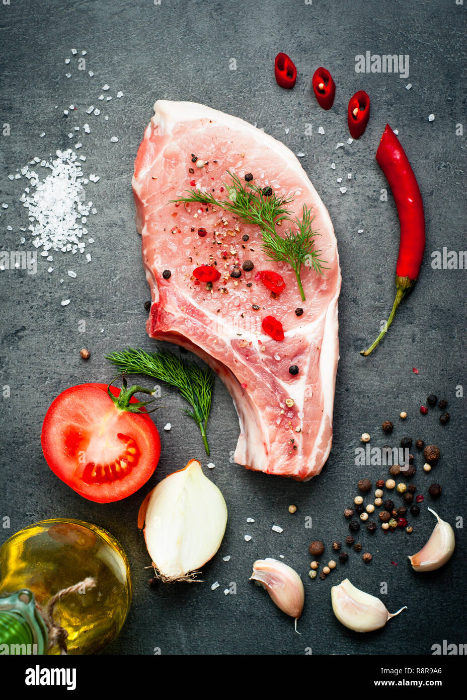 Raw pork meat on a dark gray surface and ingredients for cooking. Food background. Stock Photo