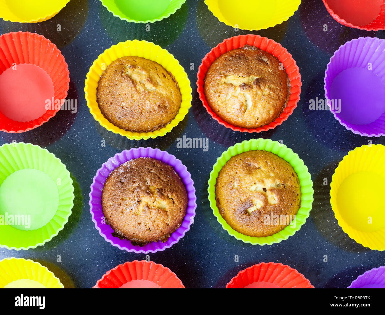 top view of four baked cupcakes in multicolored silicone molds on dark tray Stock Photo