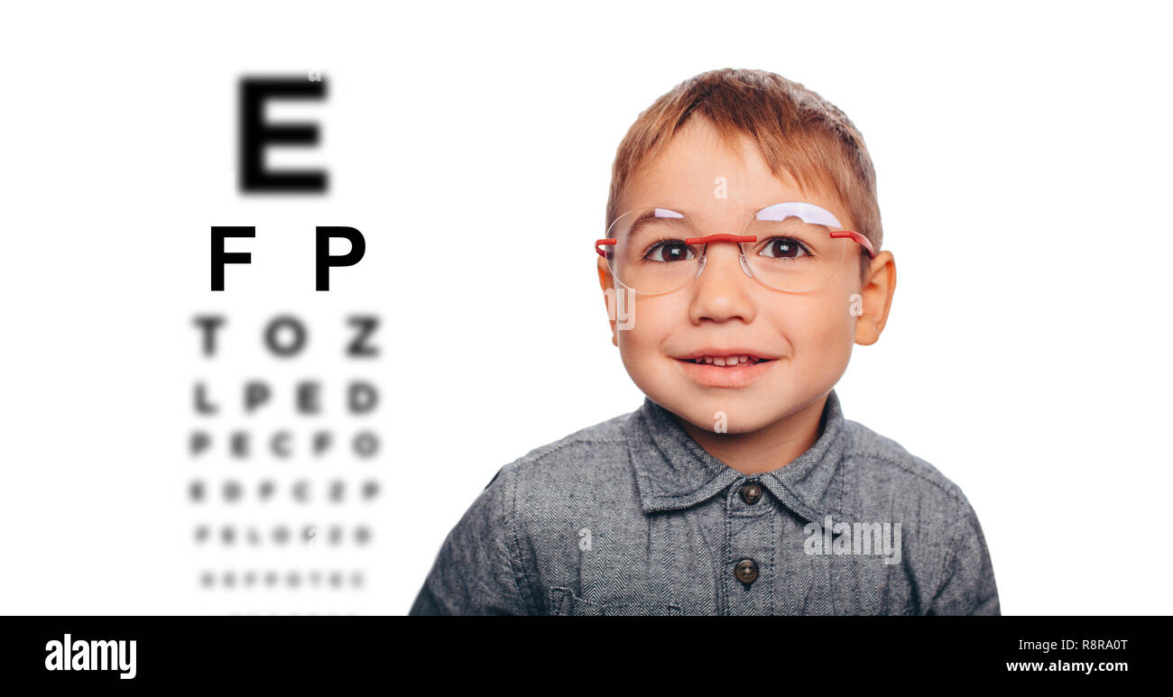 Little boy adjusting his new eyeglasses, on the eye chart background. Vision correction for children Stock Photo