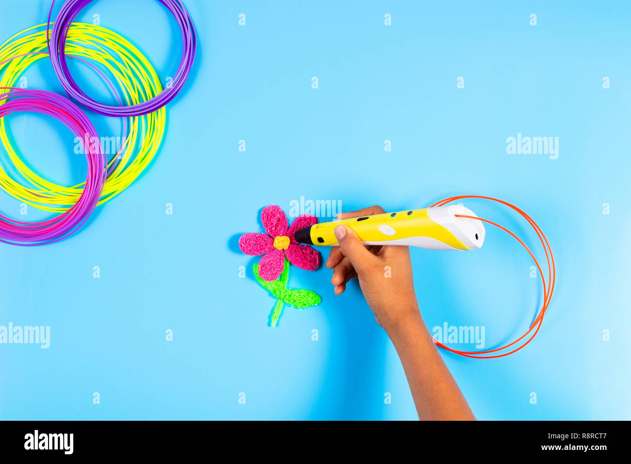 Kid hand creating with 3d pen with plastic filament on blue background Stock Photo