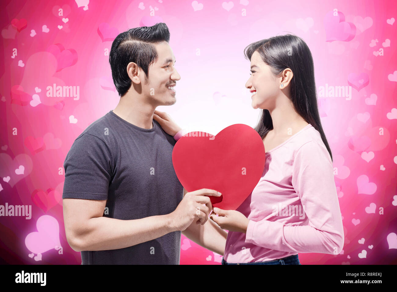 Young asian couple holding red heart shape and looking at one another ...