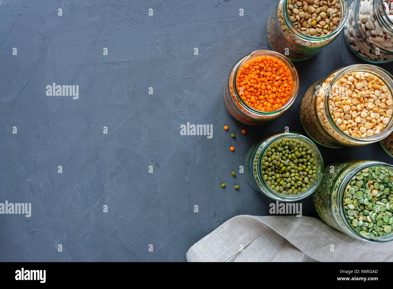 Dried legumes in storage jars on mottled blue background viewed from above with lentils, peas
