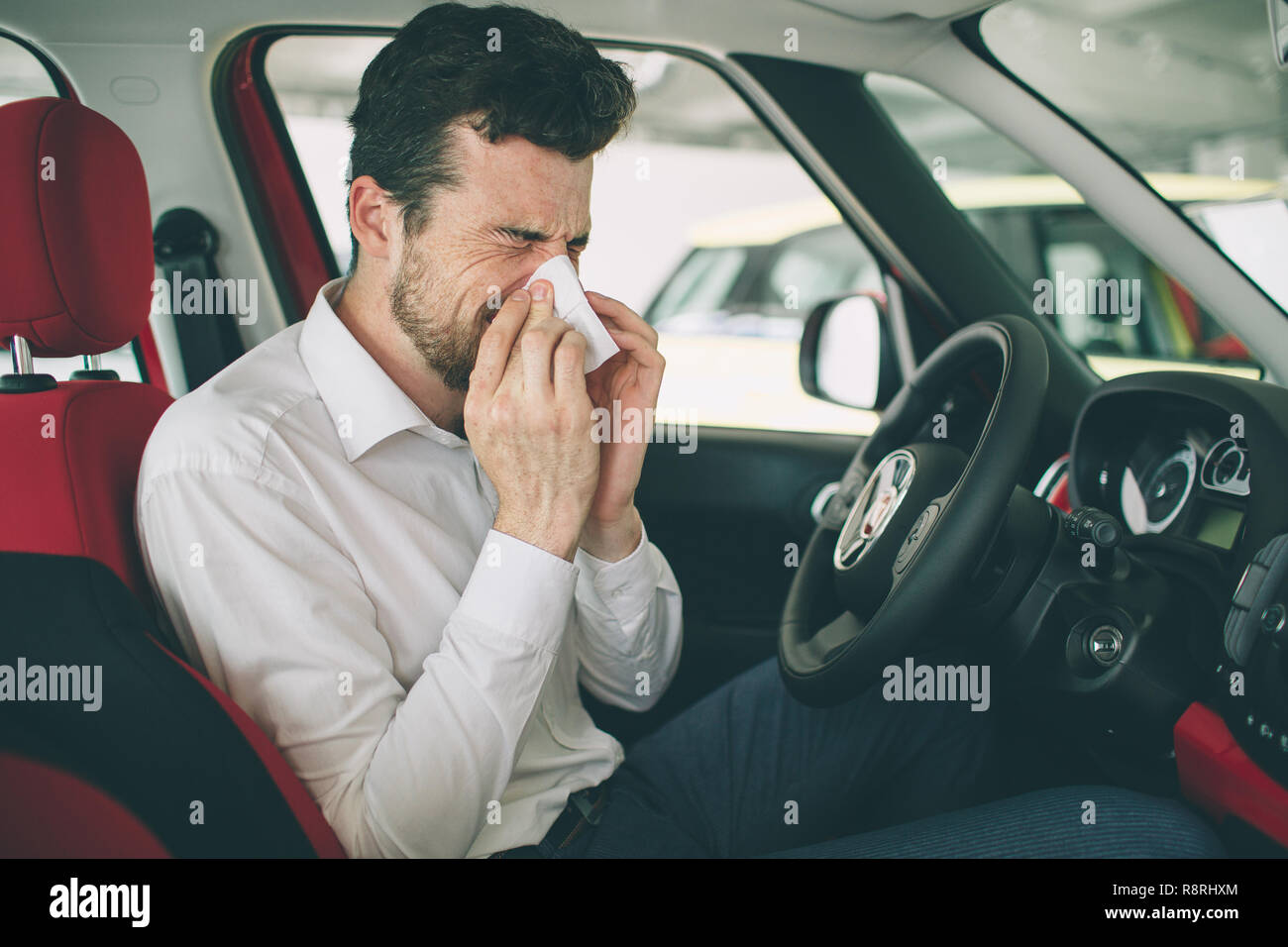 from a young man with handkerchief. Sick guy has runny nose. man makes a cure for the common cold in the car Stock Photo
