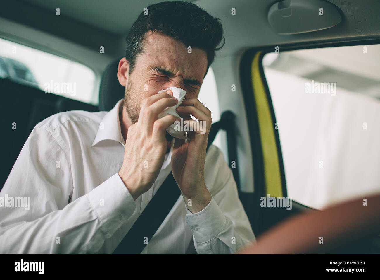from a young man with handkerchief. Sick guy has runny nose. man makes a cure for the common cold in the car Stock Photo
