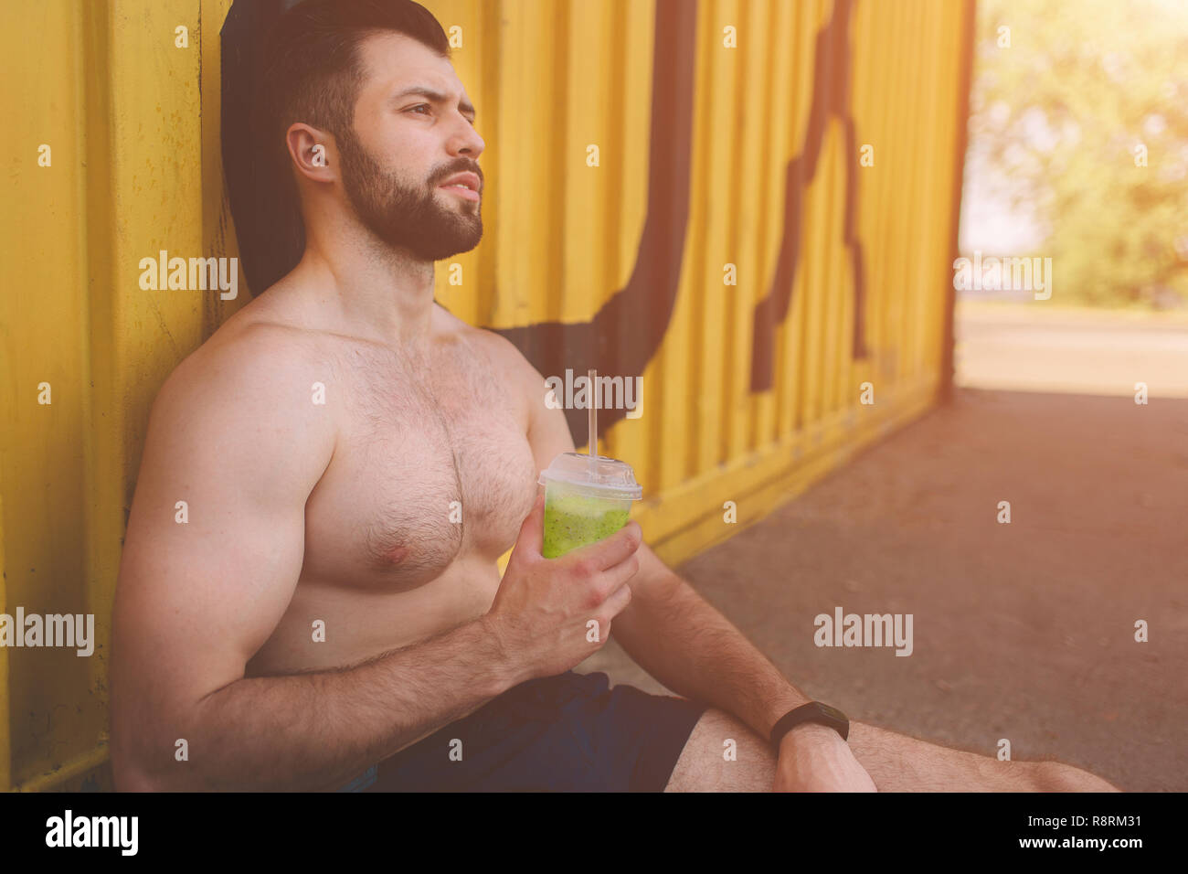 handsome young muscular man drinks Green detox smoothie cup. Picture of a young athletic man after training. Stock Photo