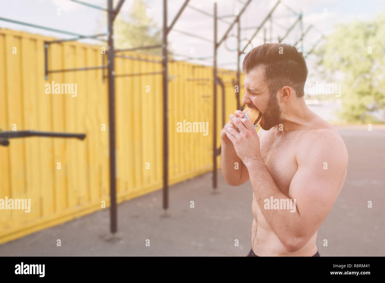 Man eats a hamburger after a workout. Very hungry, fatty and unhealthy food. Stock Photo