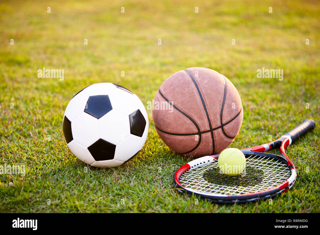 football soccer ball basketball tennis ball and racket laid on grass at sunset Stock Photo