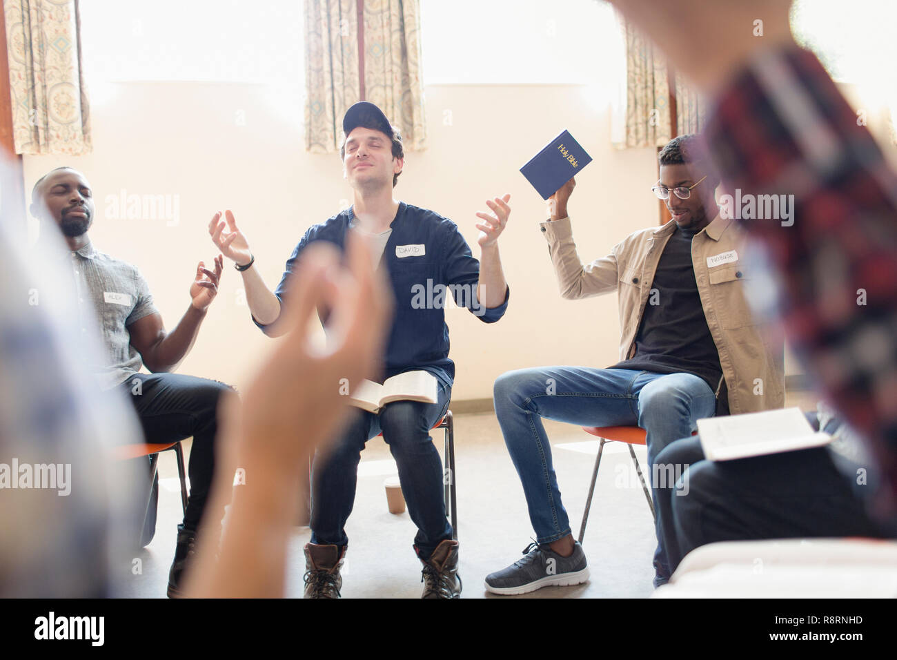 Men with bible praying with arms raised in prayer group Stock Photo