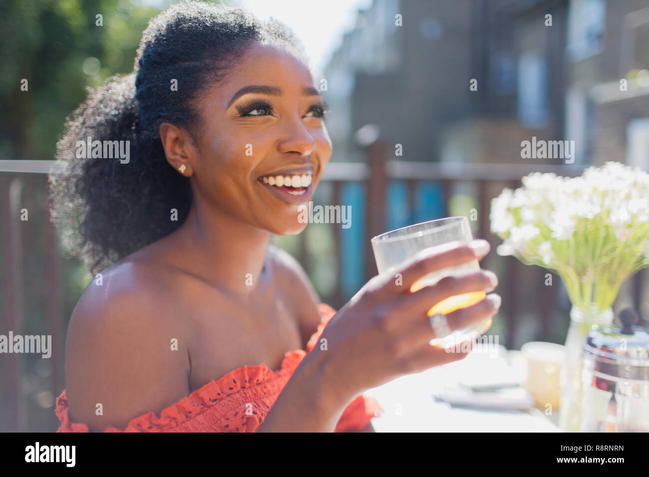 Happy young woman drinking orange juice on sunny balcony Stock Photo