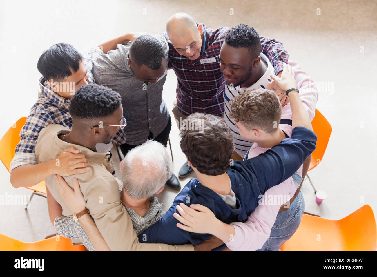 Men hugging in huddle in group therapy Stock Photo