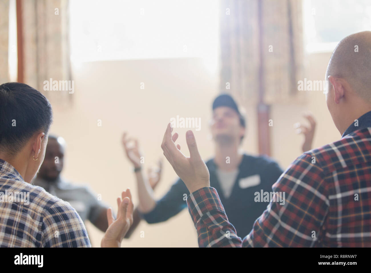 Men with arms raised praying in prayer group in community center Stock Photo