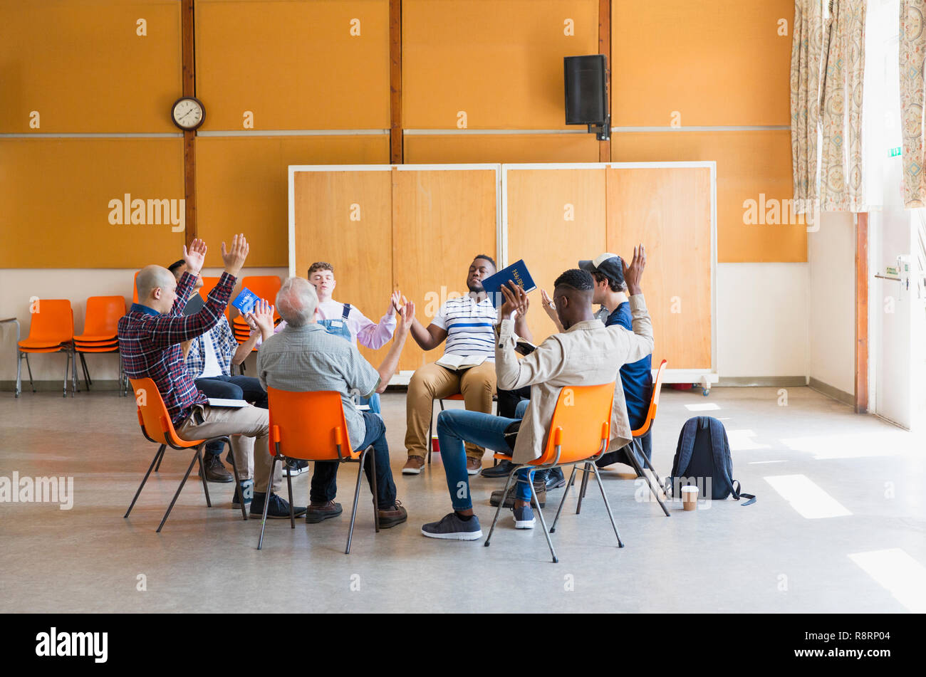 Men praying with arms raised in prayer group in community center Stock Photo