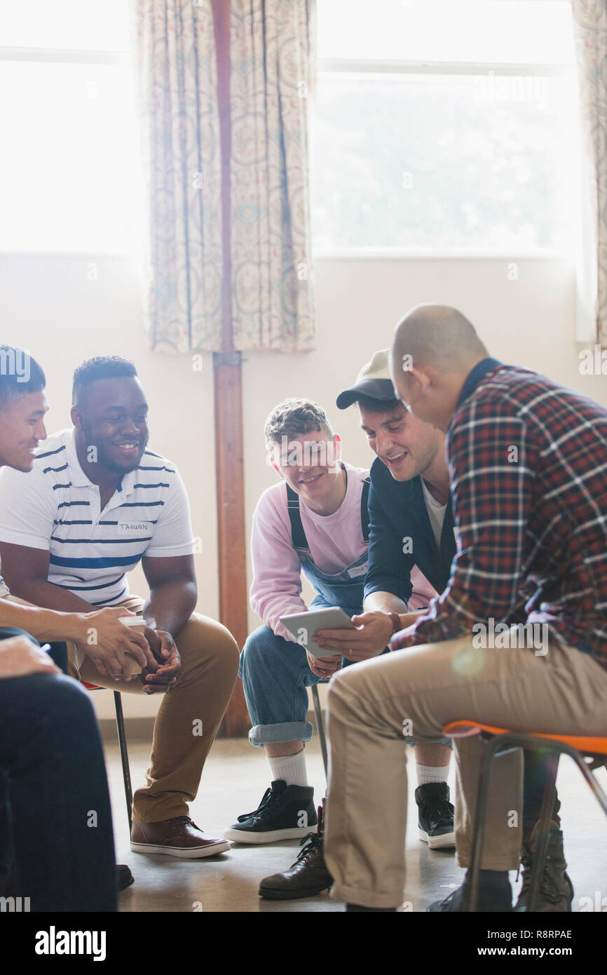 Men with digital tablet talking in group therapy circle Stock Photo