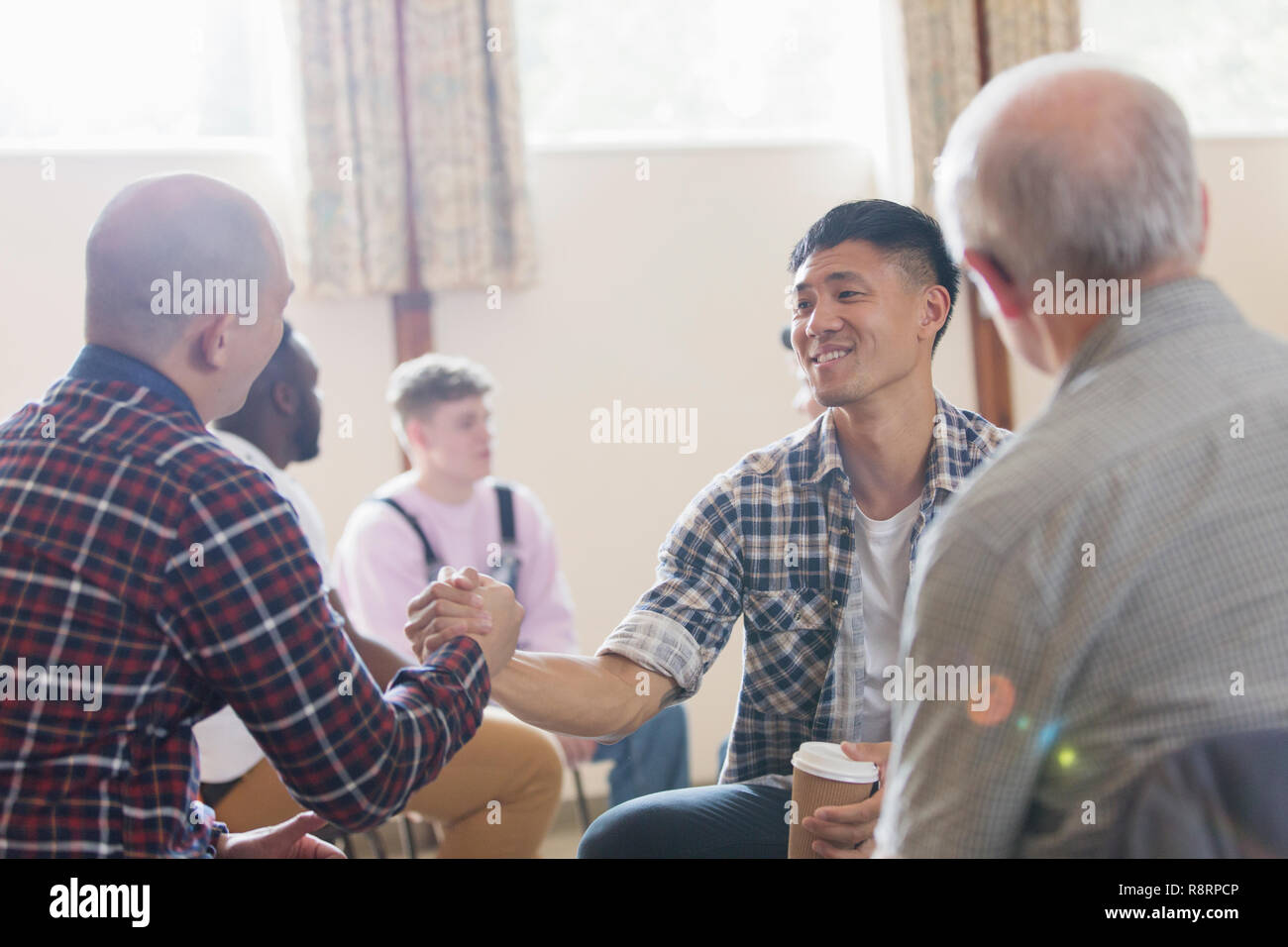 Men shaking hands in group therapy in community center Stock Photo