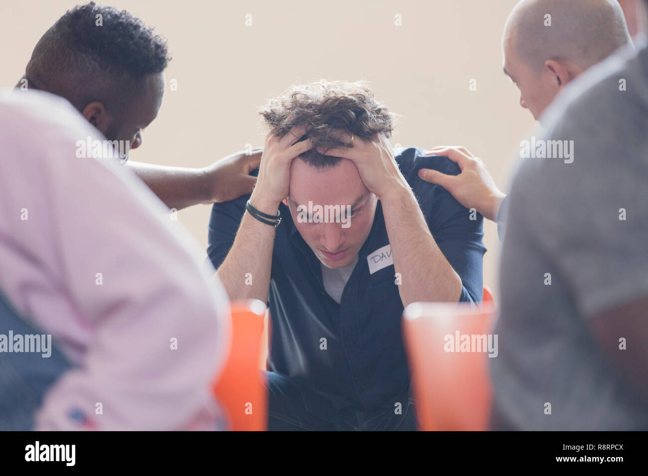 Men comforting upset man in group therapy Stock Photo