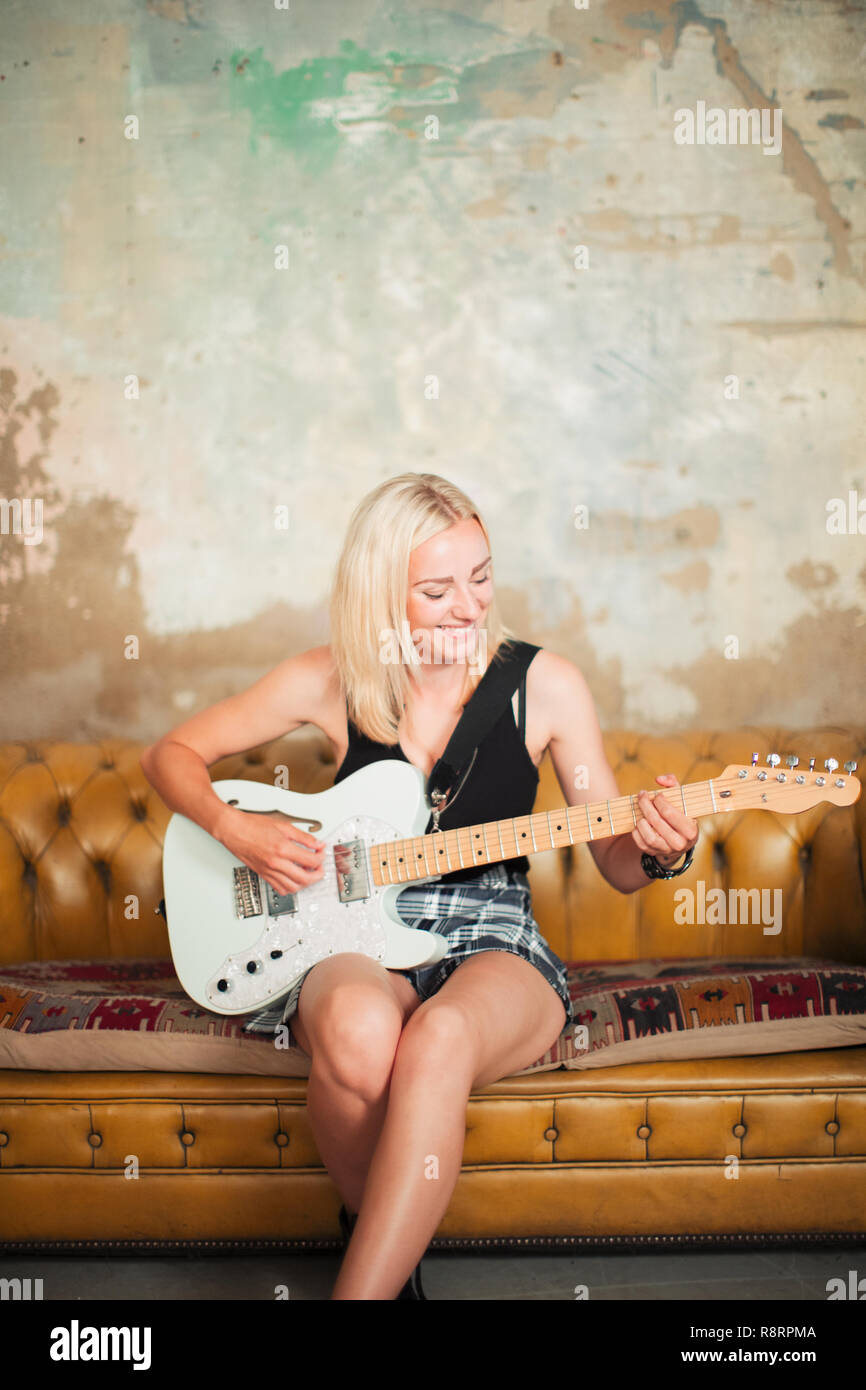 Young woman playing electric guitar on sofa Stock Photo