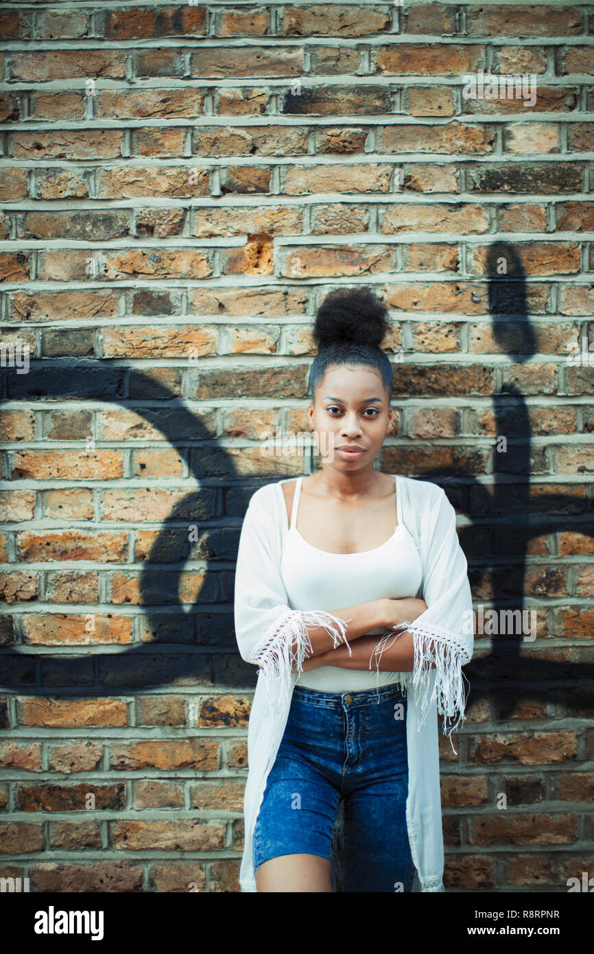 Portrait confident, serious young woman leaning against brick wall Stock Photo