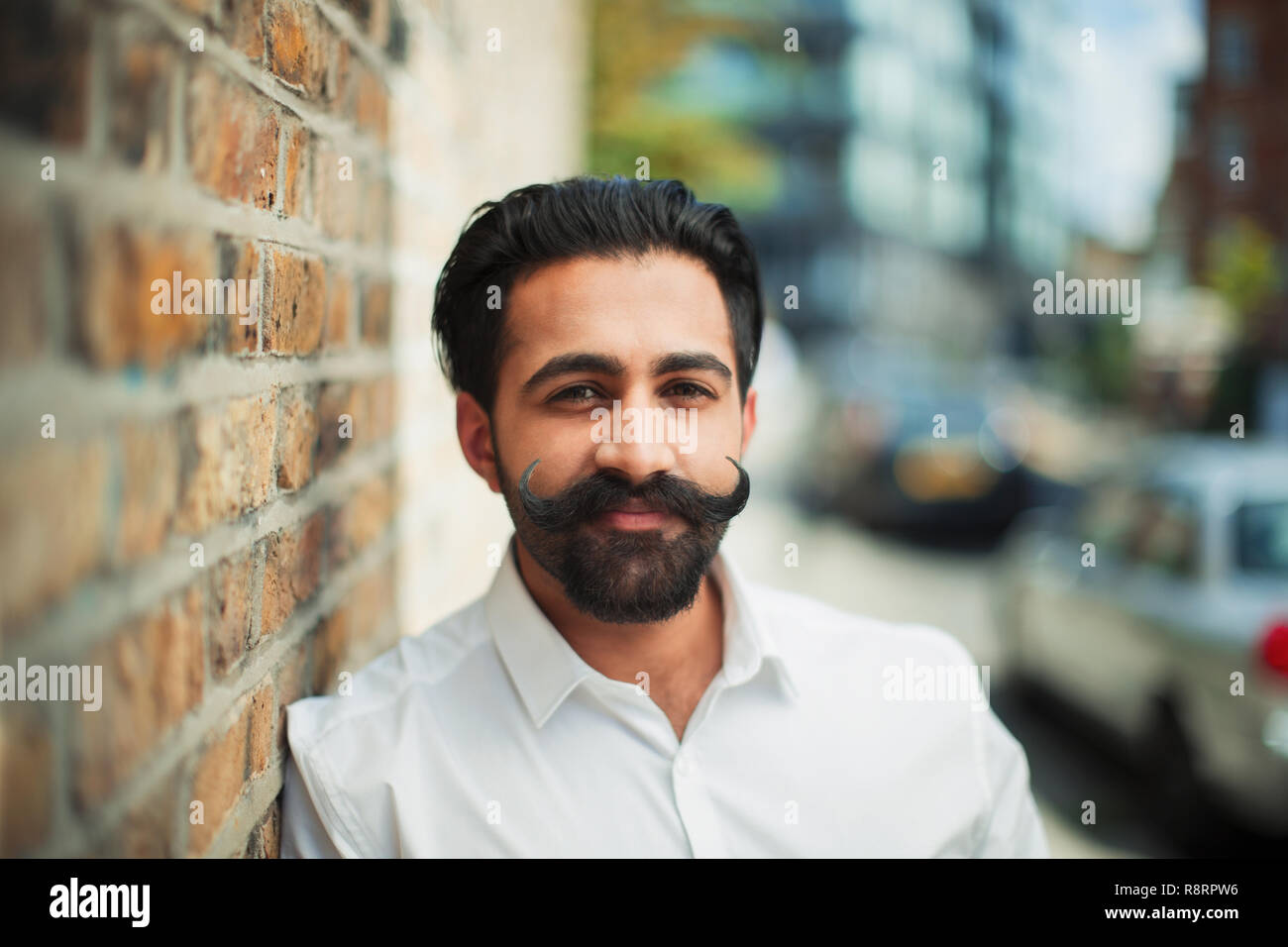 Portrait confident young man with handlebar mustache on urban sidewalk Stock Photo