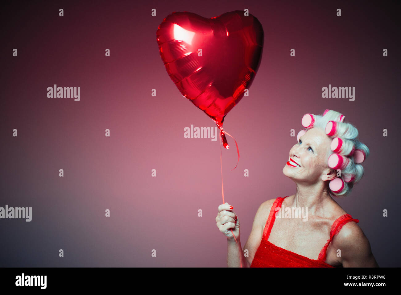 Portrait smiling senior woman with hair in curlers holding heart-shape balloon Stock Photo