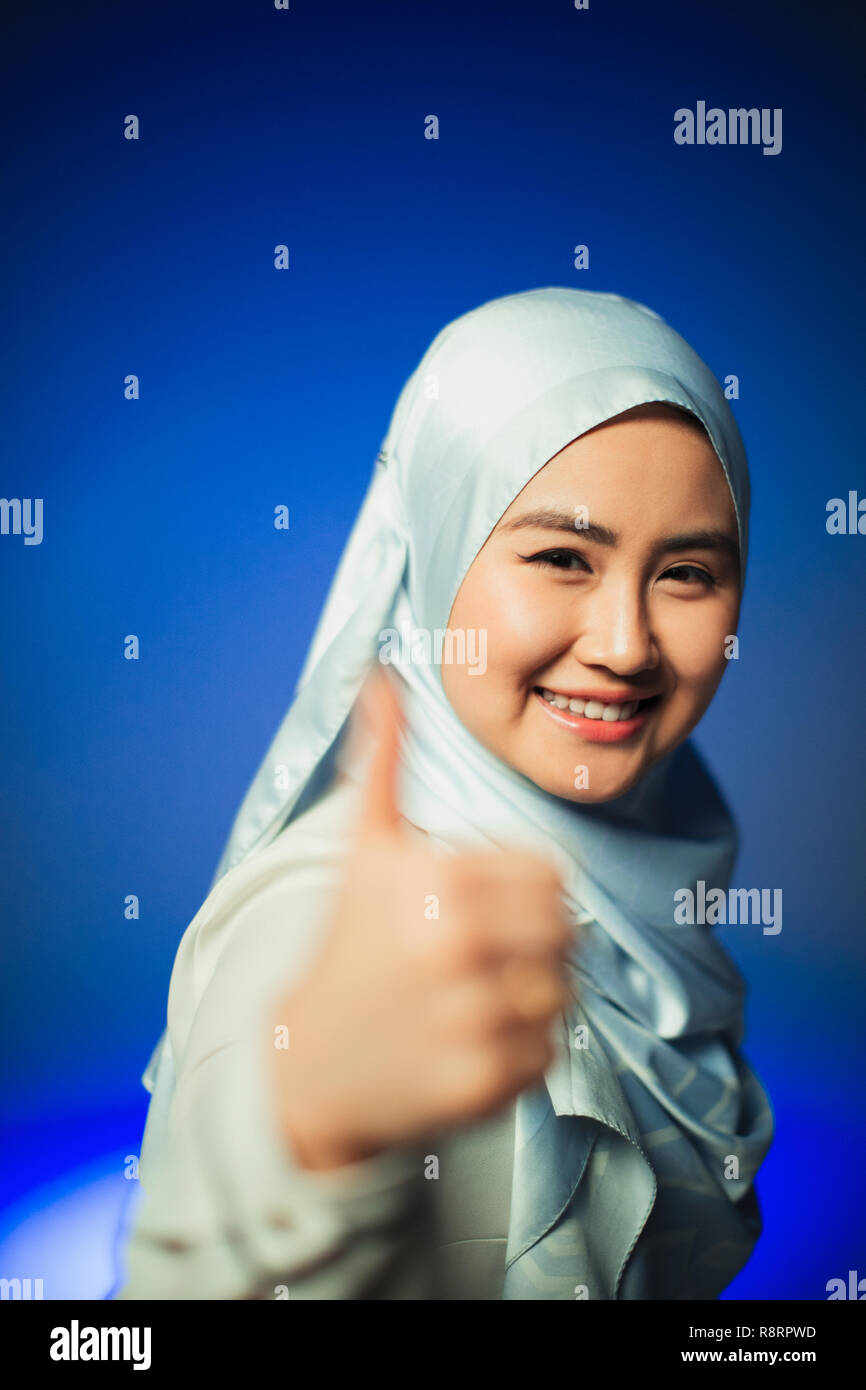 Portrait smiling, confident young woman in blue silk hijab gesturing thumbs-up Stock Photo