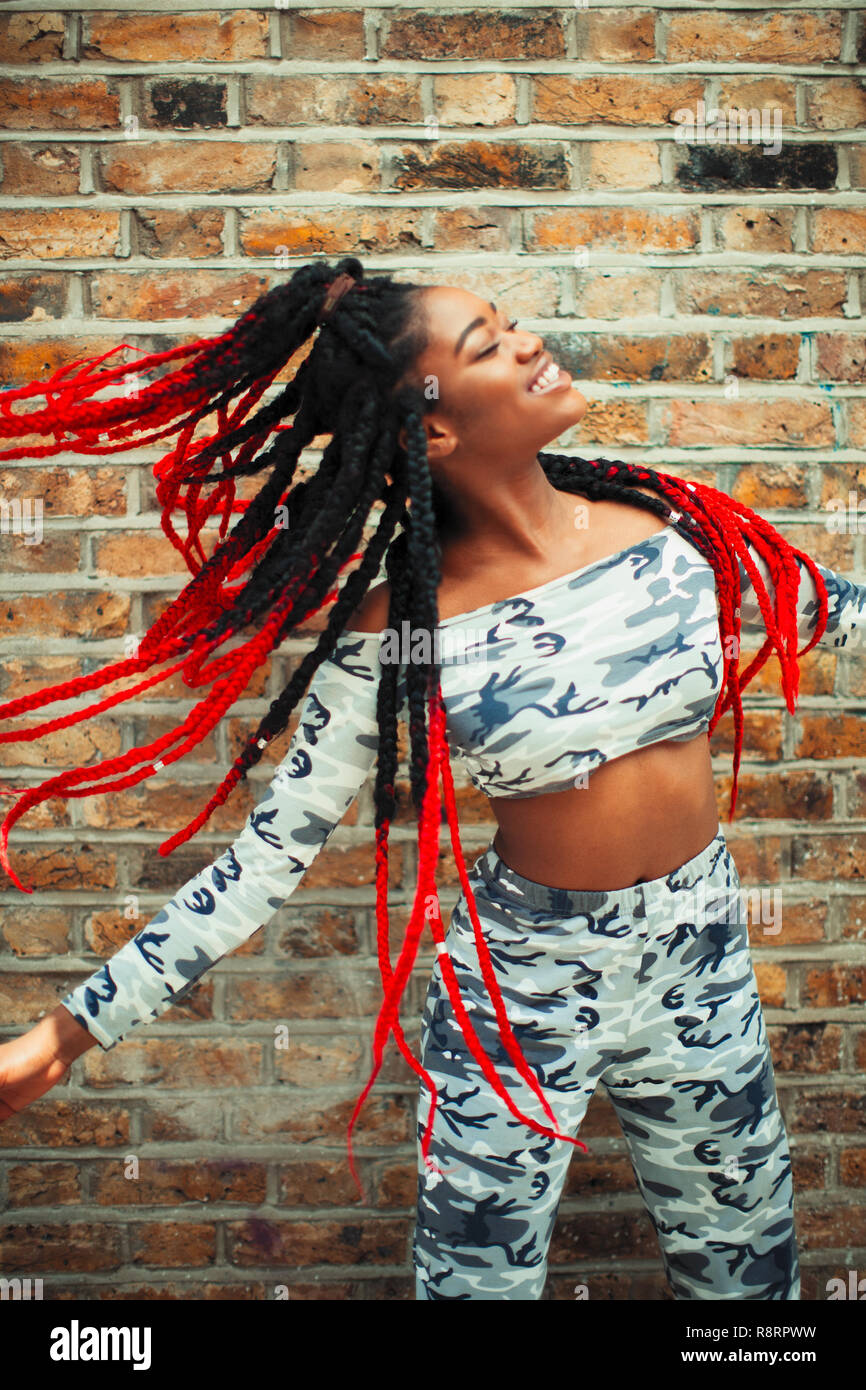 Carefree young woman in camouflage clothing dancing against brick wall Stock Photo