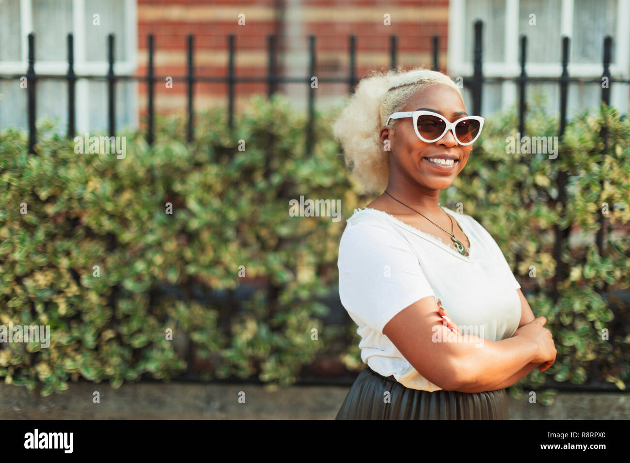 Portrait smiling, confident young woman in sunglasses on urban sidewalk Stock Photo