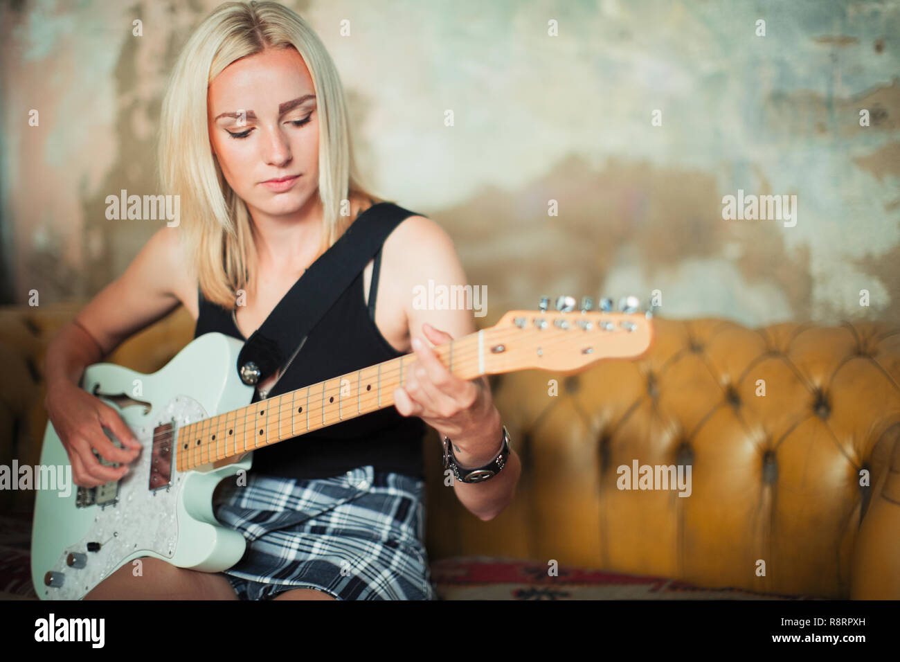 Young woman playing electric guitar on sofa Stock Photo