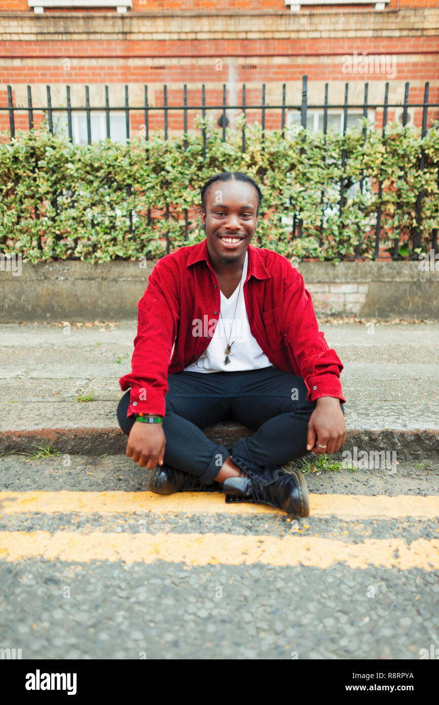 Portrait smiling, confident teenage boy sitting on urban curb Stock Photo