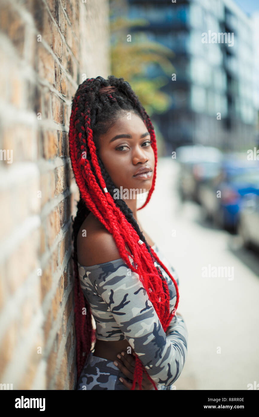 Portrait confident young woman with long red braids on urban sidewalk Stock Photo