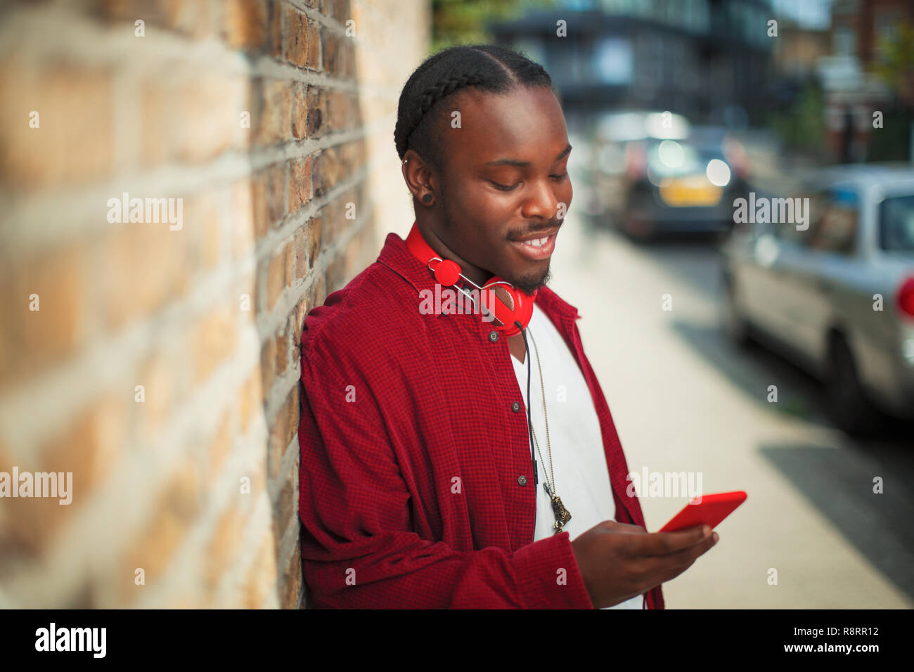 Smiling teenage boy with headphones using mp3 player on urban sidewalk Stock Photo