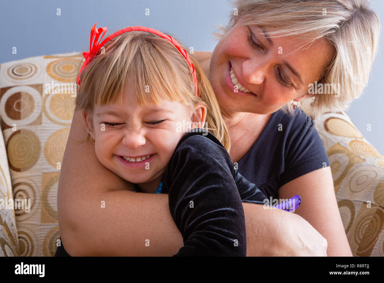 Fun happy loving mother and daughter enjoying a laugh and cuddle as the relax together in a comfortable armchair at home Stock Photo