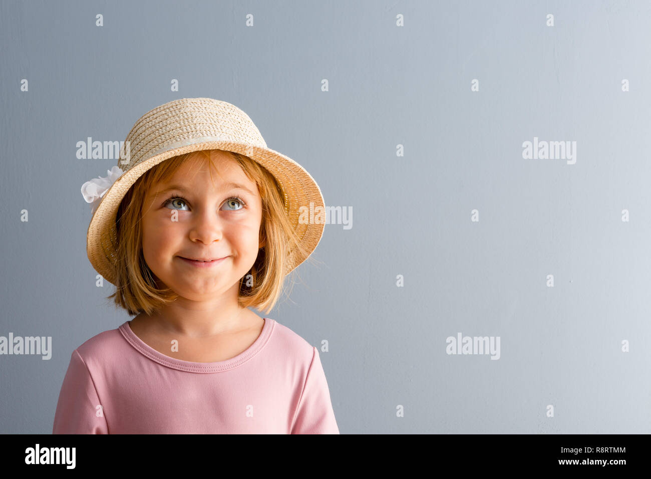 Cute little blond girl daydreaming with a happy smile looking up into the air letting her imagination run free over a blue background with copy space Stock Photo