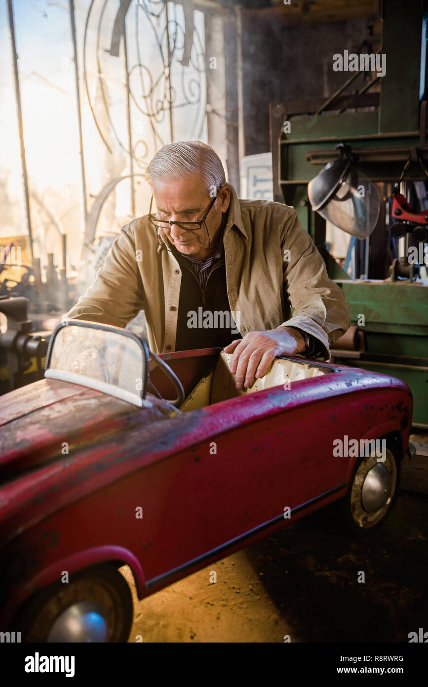 Senior man in his workshop repairing an old fashioned pedal car  Stock Photo