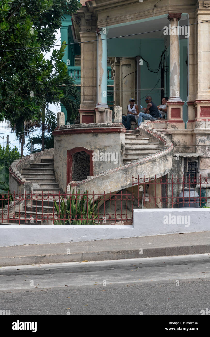 Three Cuban men chatting on the terrace of an old dilapidated Cuban house with amazing curved staircase. Havana Cuba Stock Photo