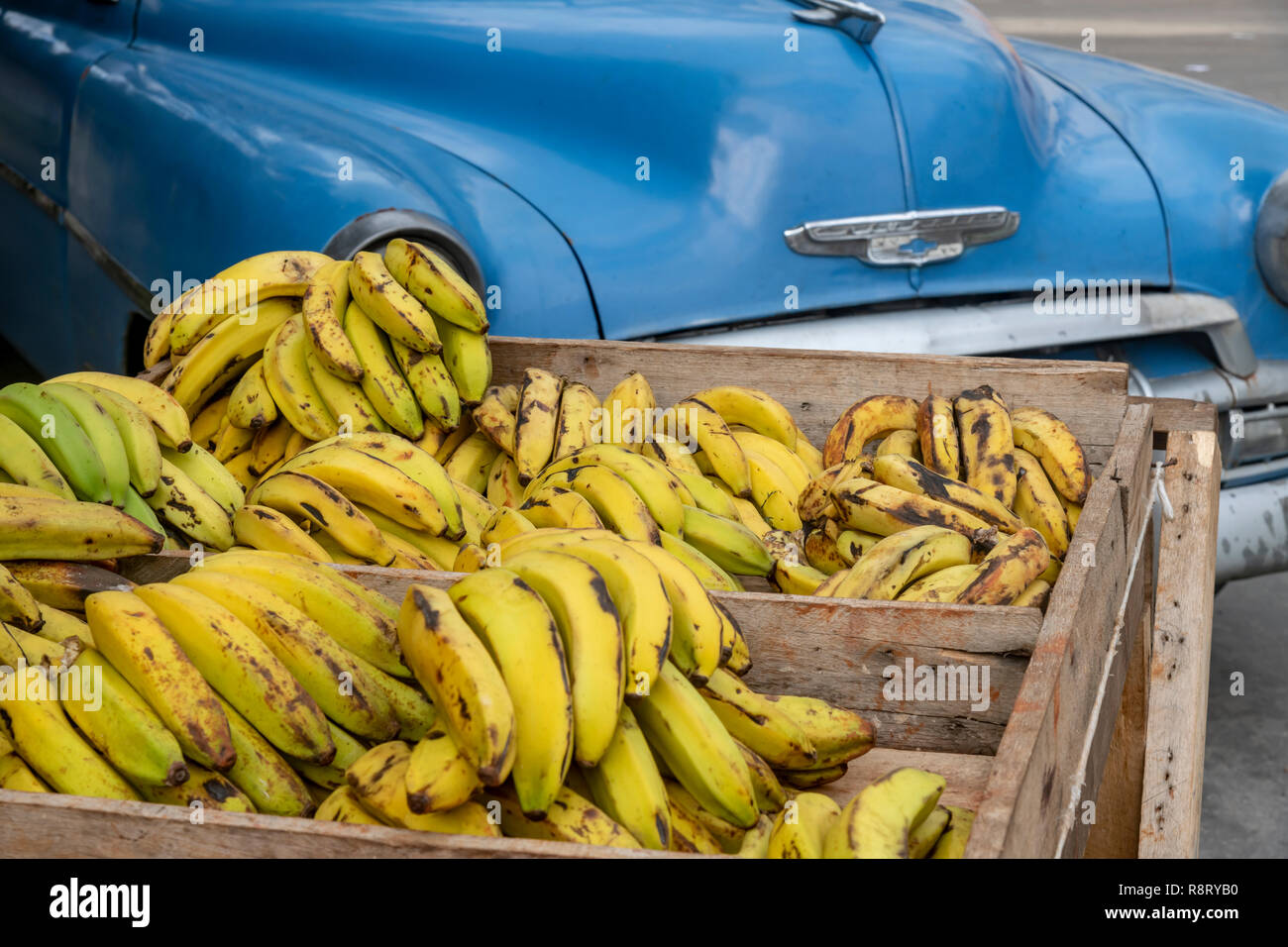 Crates of bananas for sale in front of old blue American Chevrolet car, on the corner of Lugareño and Ayestarán streets in Havana, Cuba. Stock Photo