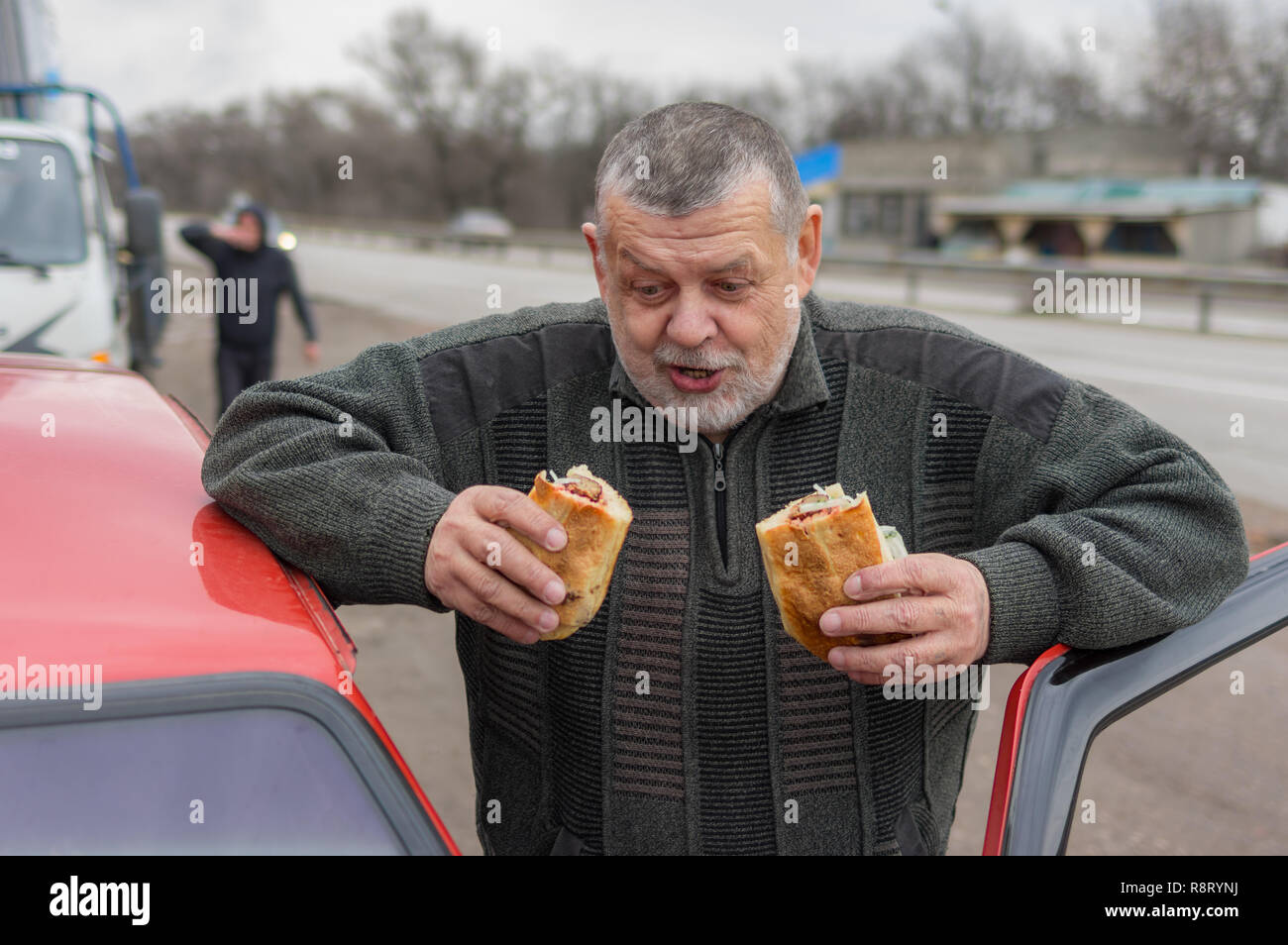 Portrait of Caucasian hungry senior driver ready to eat street food near his car Stock Photo