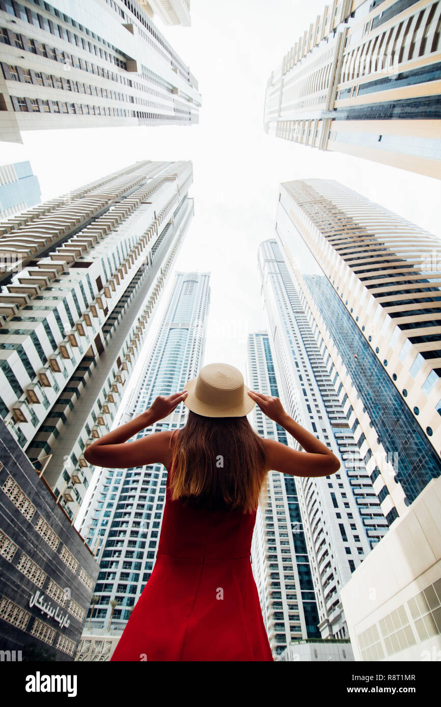 Rear view of young woman in red dress holding with both hands straw hat ...