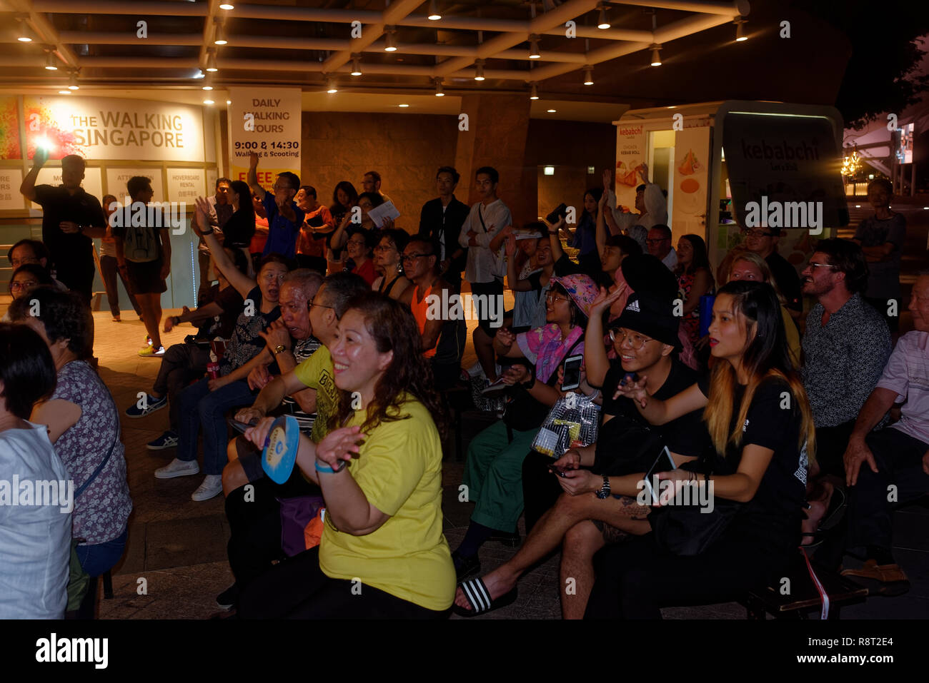 Enthusiastic audience clapping and cheering karaoke singer along the Esplanade walk in Singapore Stock Photo