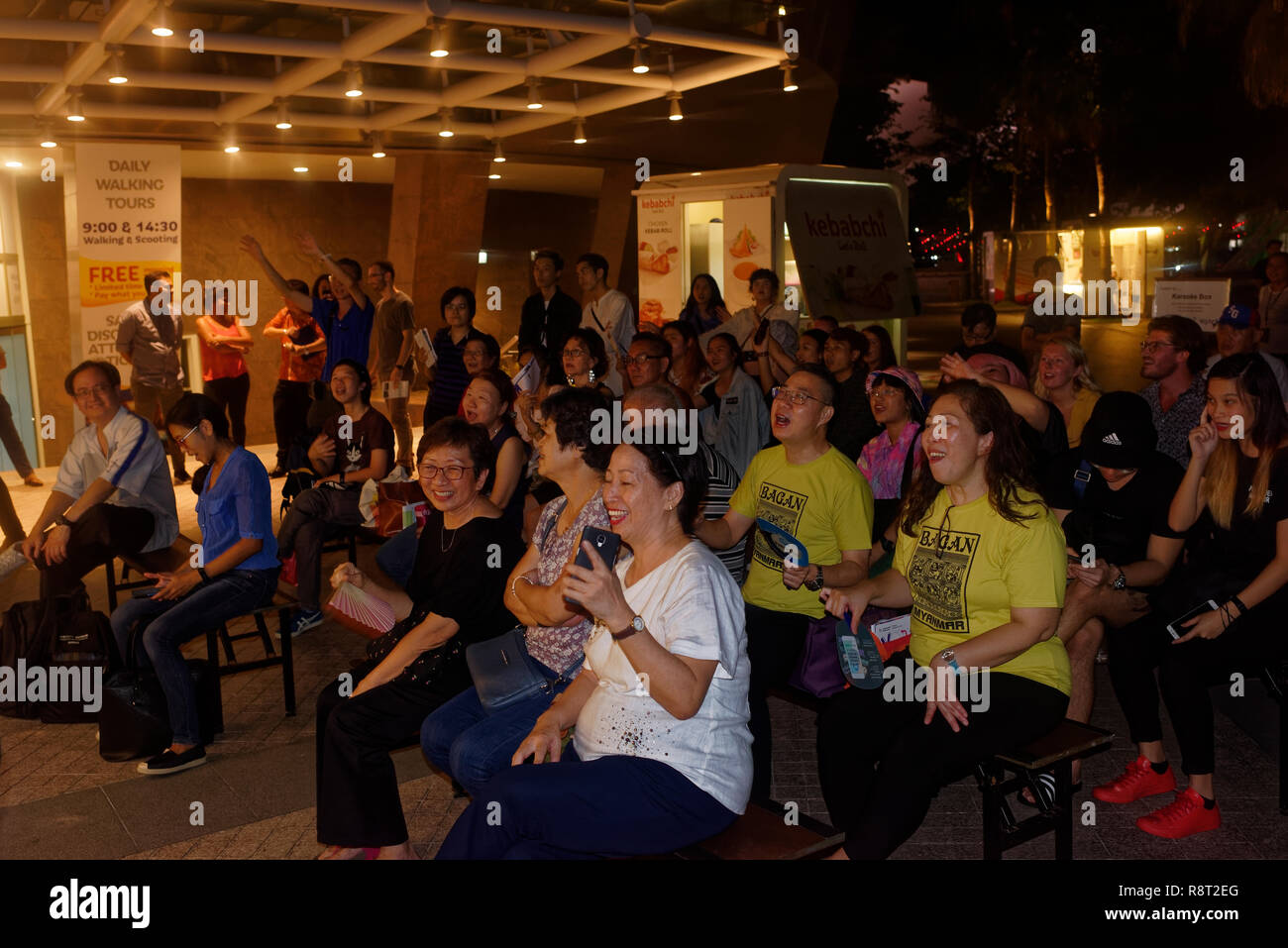 Enthusiastic audience clapping and cheering karaoke singer along the Esplanade walk in Singapore Stock Photo