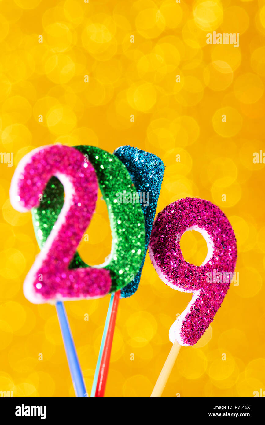 closeup of some glitter numbers of different colors forming the number 2019, as the new year, on a bright yellow background, with some blank space on  Stock Photo