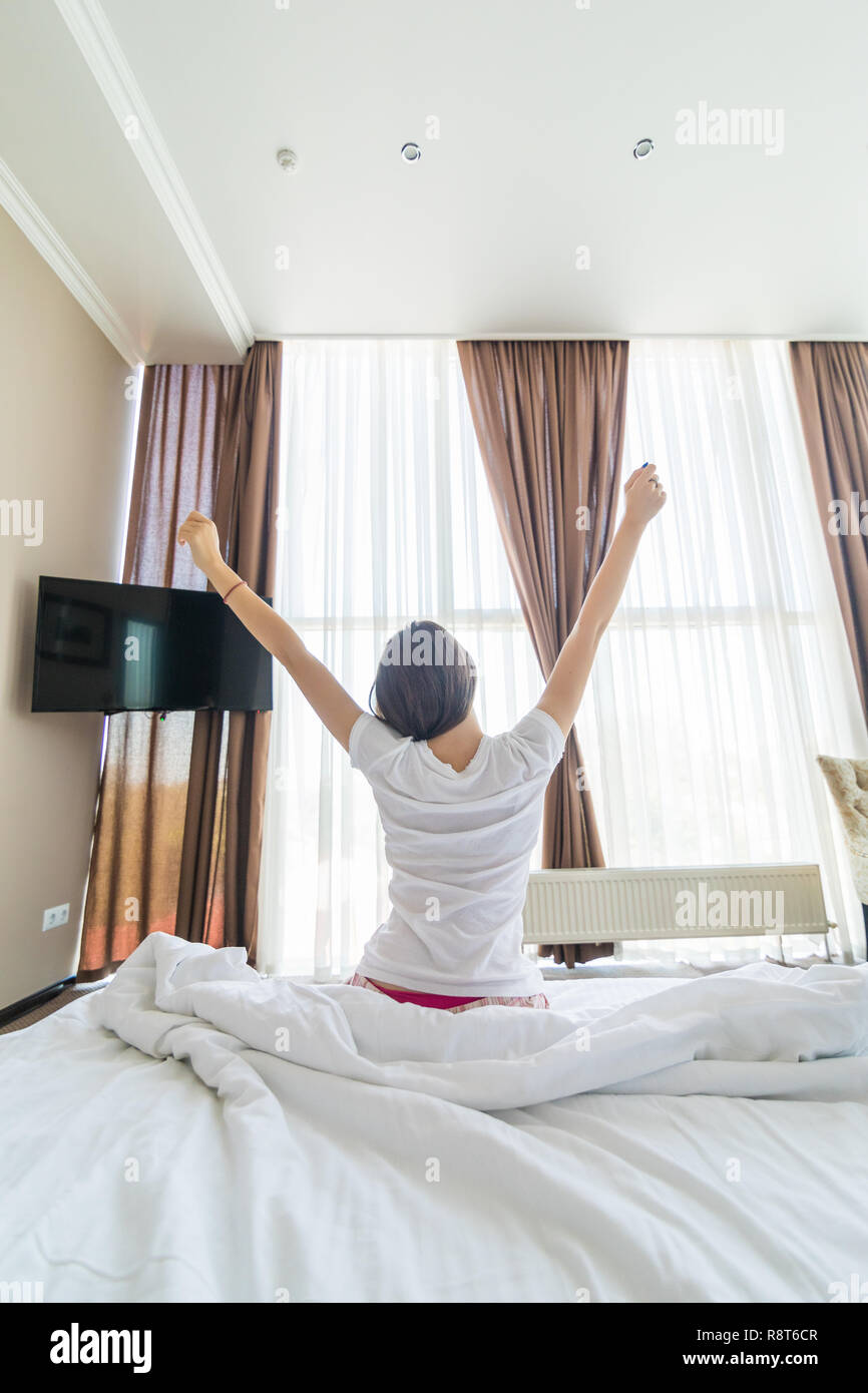 Young pretty woman outstretching her arms sitting on the bed after good ...