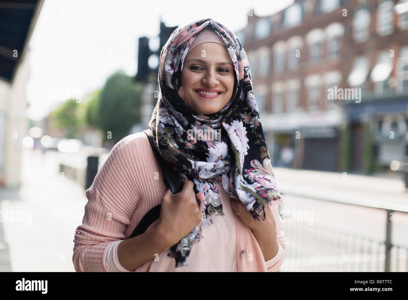 Portrait smiling, young woman wearing floral hijab on urban sidewalk Stock Photo