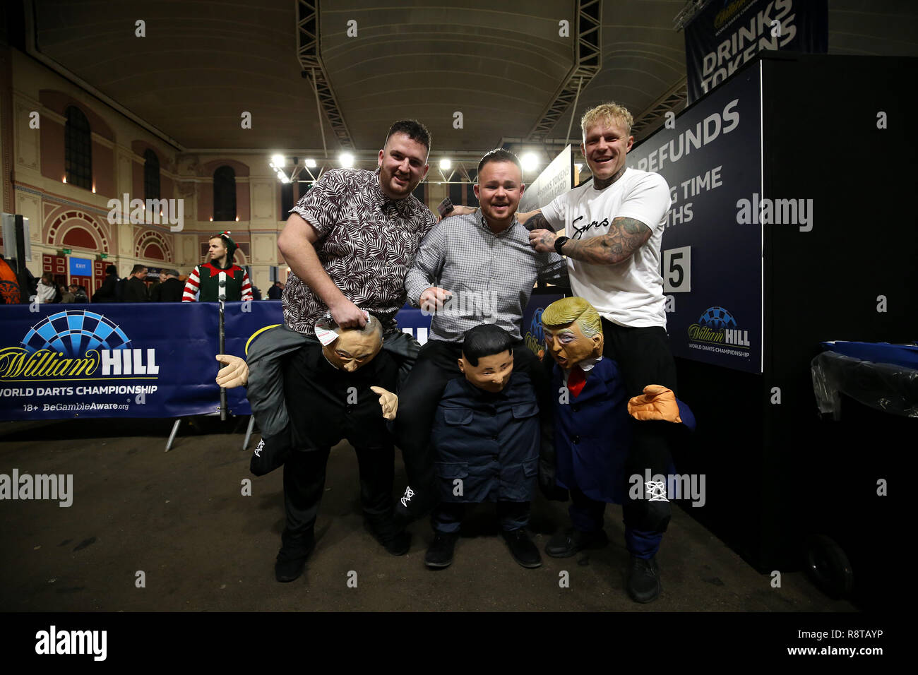 Fans wearing Russian President Vladimir Putin, North Korea President Kim Jong-un and President of the United States Donald Trump costumes during day five of the William Hill World Darts Championships at Alexandra Palace, London. Stock Photo