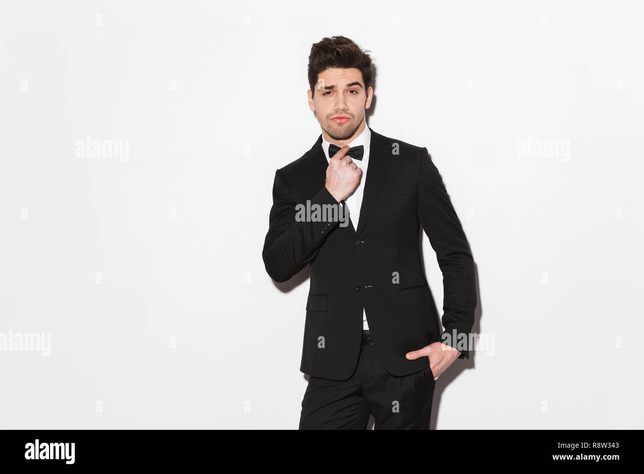 Portrait of a handsome young man wearing black suit with a bow standing ...