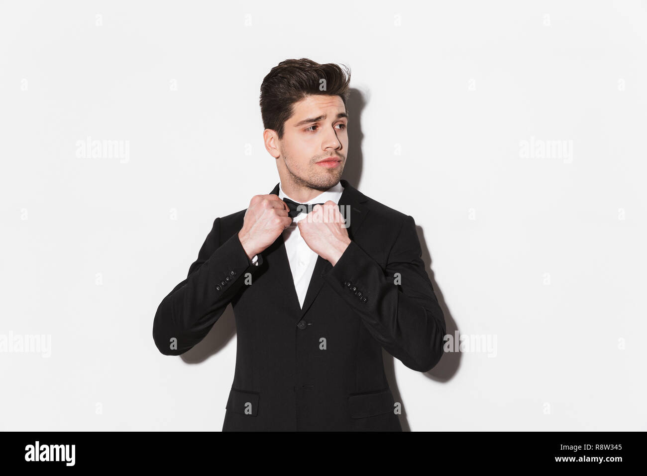 Portrait of a handsome young man wearing black suit with a bow standing ...